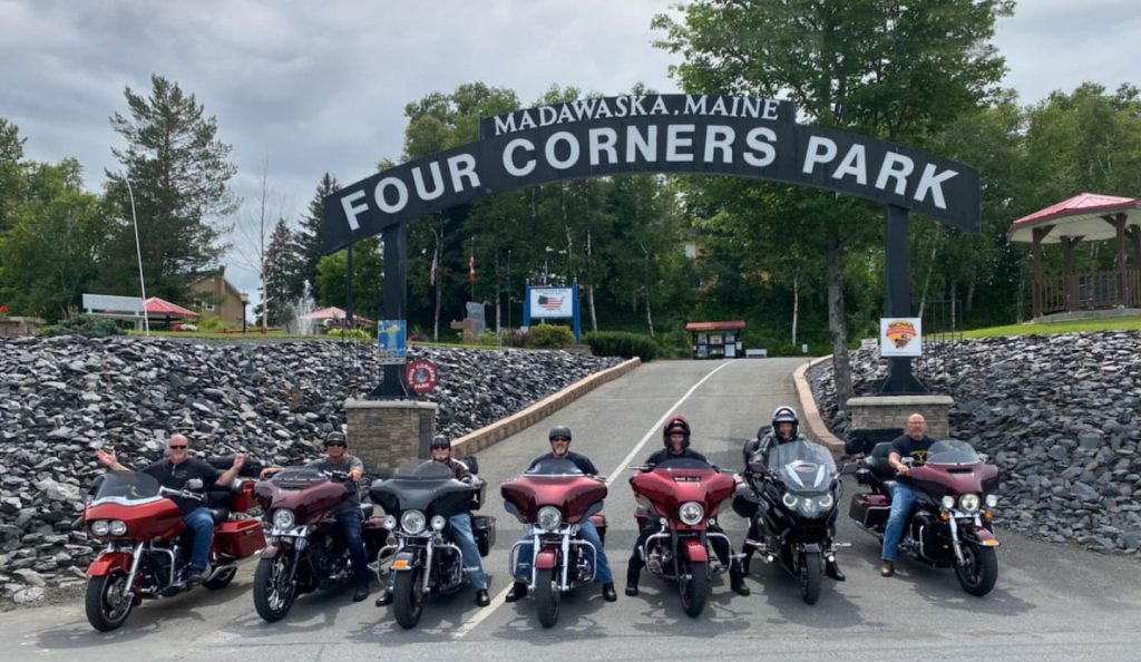 Photo of bikers in from of the sign for the Four Corners Park in Madawaska, Maine